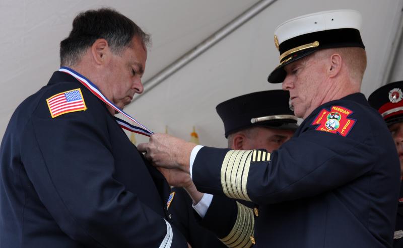 Wareham Fire Chief Robert McDuffy places a medal around the neck of Captain Edwin Brundage during the Braveheart Awards ceremony on Saturday, September 17. Four firefighters were recognized for saving the life of a teen who was trapped in a burning vehicle after it crashed into a home. BY JAIME REBHAN