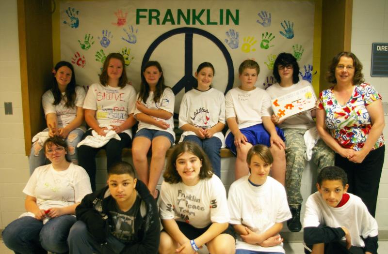 Wareham Middle School's peace team in front of artwork they made featuring a peace sign and handprints with messages inscribed in them on June 14 at the middle school. From left to right, top row: Samantha Liebgott, Noelle Jackson, Kelsey Edwards, Lauren Timmons, Devon Martin, Shawn Wasilowski, and School Psychologist and Team Founder Kathy Lyons. Bottom row: Adrianna Burgess, Angel Padilla, Alexis Adams, Spencer Boyer, and Louis Haskell. BY RISHI SIDHU