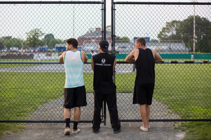 From left to right, Kyle Hayes, 20, Matt Ingargiola, 21, and Greg Cummings, 20, watch the beginning of the game through a fence. BY CAROLYN BICK