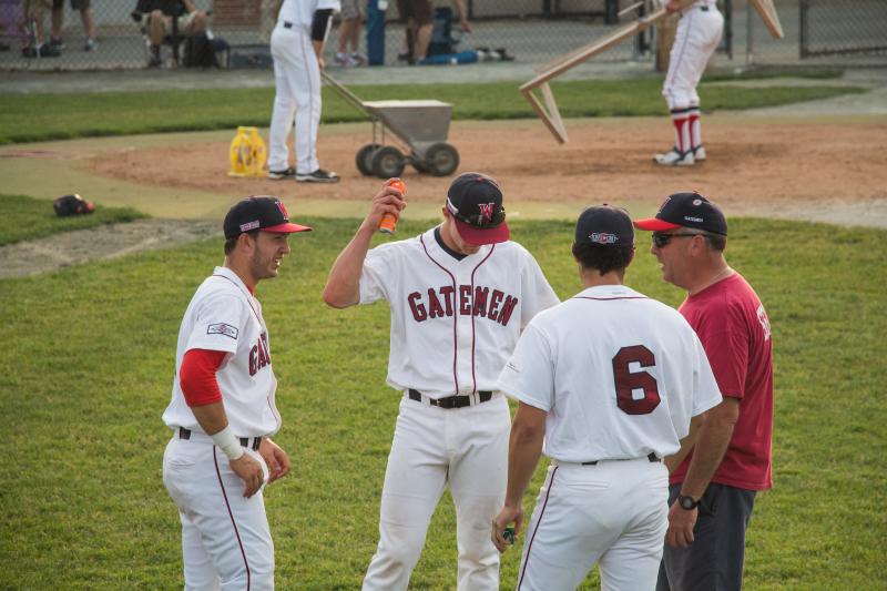 A Gatemen player sprays himself with bug spray, while others prepare the field for play, behind him. BY CAROLYN BICK