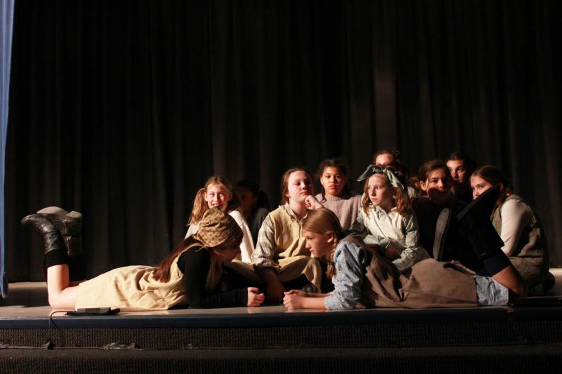 The orphans (Cassidy Bridge, Sydney Draper, Makayla Semiao, Jordyn Morrell, Ashley Moran, Addyson Pimental, Hehvin Barnett, Julia Bottino, Nadiya Dows, Daelyn Corbin, and Fredi Gakidis) sit around a radio and listen to Oliver Warbuck’s search for Annie’s parents. BY ZARRIN TASNIM AHMED