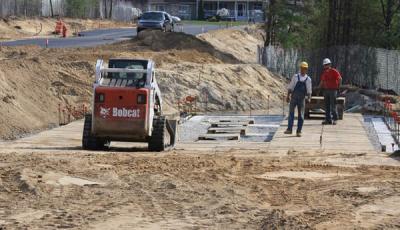 A Bobcat brings cribbing to the semi-completed foundation at the building's new site. The fireplace and windows will be on the left, facing the street and a common area across the street. BY JAIME REBHAN