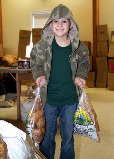 Ben Bailey, 7, helps lug the five-pound bags of potatoes that went into each box. BY ANDREW W. GRIFFITH