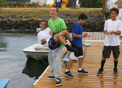 Boys and Girls Club youth staff Christopher Jesus mock throws 11-year-old Evan Kyle into the water after a morning of rowing in New Bedford Harbor. BY RISHI SIDHU