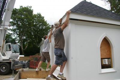 Jim Meckes, a volunteer maintenance man with the church (right), and Michael Willliams nudge the roof of the bell tower into place before its taken up by the crane. BY RISHI SIDHU