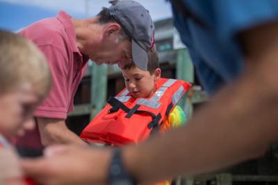 A man helps his son adjust his lifejacket, as Rob Hancock, foreground right, does the same for the man's other son, before heading out to Burgess Point. BY CAROLYN BICK