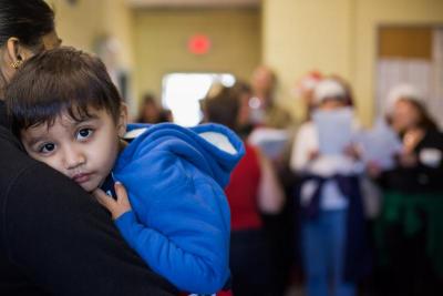 Dev Guari, 2, rests on her mother's shoulder, as carolers sing in the background at the Onset fire station. BY CAROLYN BICK