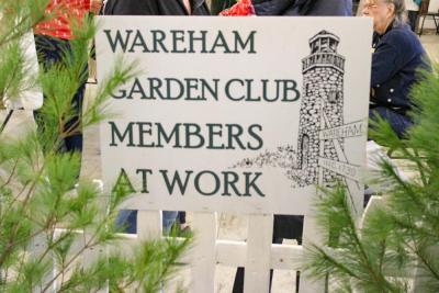 A sign at the garden club fair framed by real pine trees.