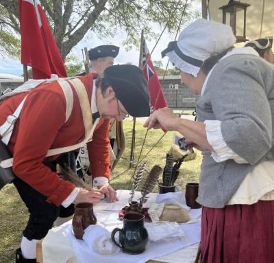 The event had people dressed in historic clothing and offering traditional activities. One booth had historic clothing and jewelry that attendants could buy, while another offered food of the time, like molasses cookies. This booth, led by Cathy Potter, allowed participants to try writing with a feather and ink.