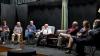 A group of actors sits on the stage during a scene in the play "The Attorney in Fact"